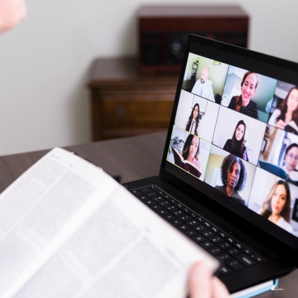 A person holds a book while participating in an online video call with a group on a laptop screen.