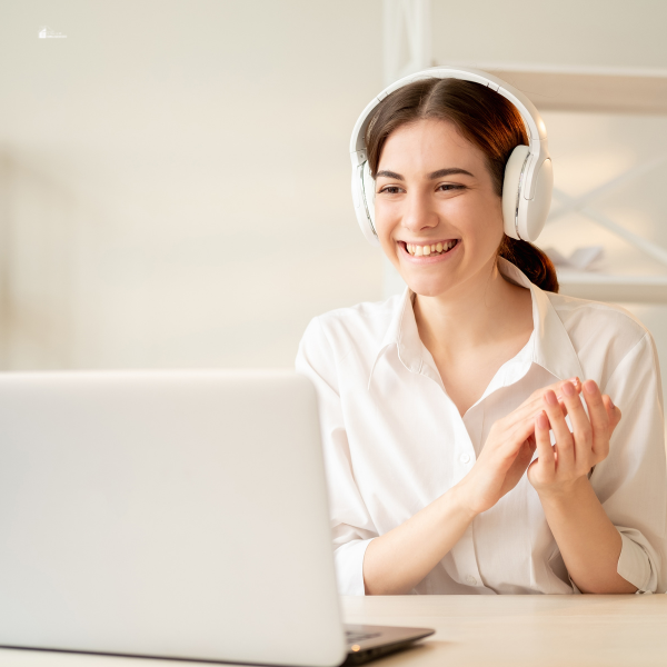 A woman wearing headphones smiles while engaging in an online video call on her laptop.