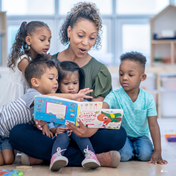 A woman reads a book to a group of young children gathered around her, engaging them in a fun learning activity.