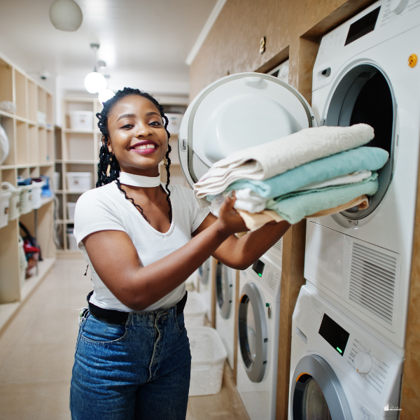 A smiling woman folds laundry at a laundromat, completing a household chore.