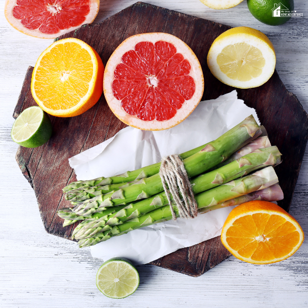 A bundle of fresh asparagus surrounded by vibrant citrus fruits on a rustic board, highlighting seasonal ingredients for delicious recipes to cook this March.