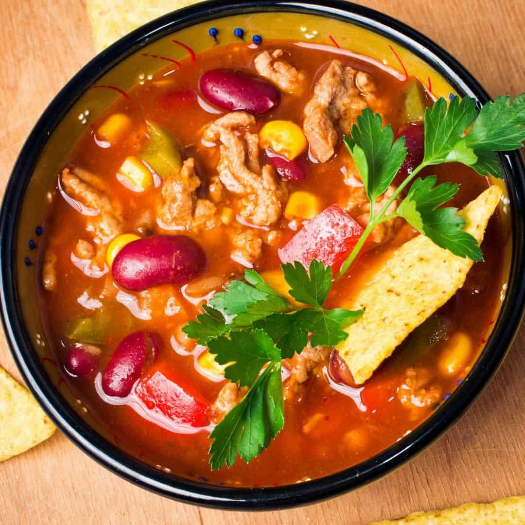 This hearty bowl of slow cooker taco soup is packed with bold Mexican-inspired flavors, featuring ground beef, kidney beans, sweet corn, and vibrant spices in a rich tomato base. Topped with fresh parsley and served with crispy tortilla chips, it's the perfect cozy meal for busy days or taco nights.