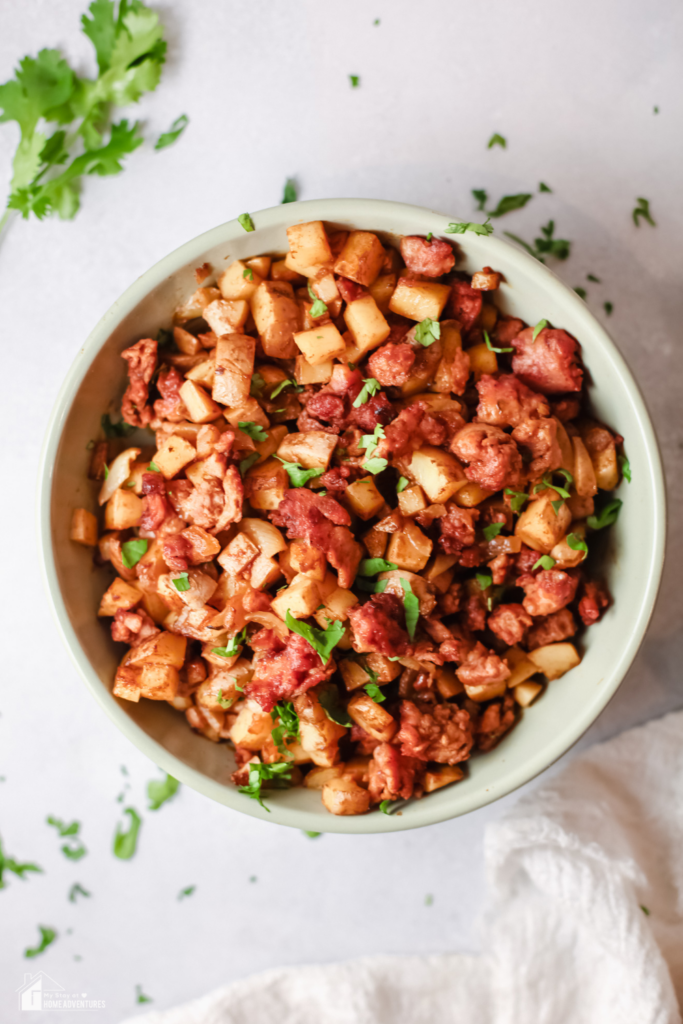 A bowl of Papas con Chorizo, a Mexican dish featuring diced potatoes and seasoned chorizo, garnished with fresh cilantro on a light background.