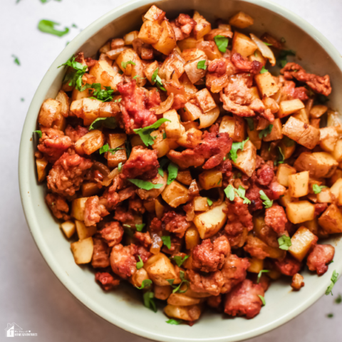 A bowl of Papas con Chorizo, a Mexican dish featuring diced potatoes and seasoned chorizo, garnished with fresh cilantro on a light background.