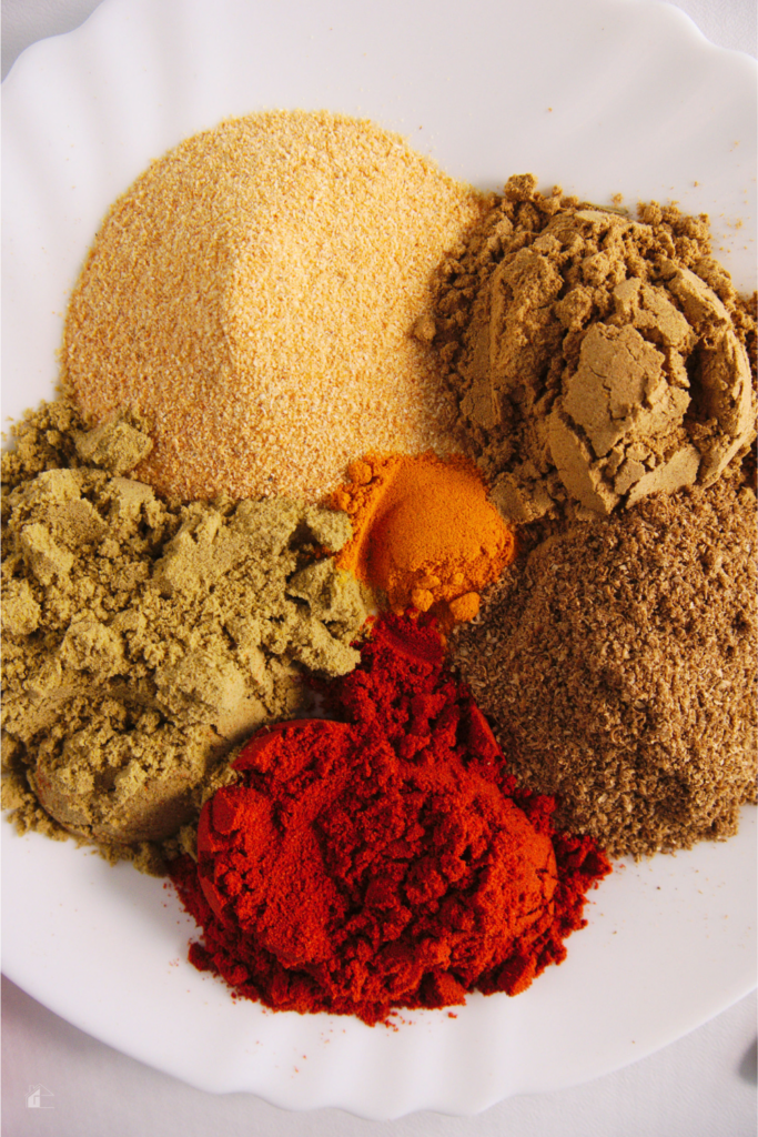 Various spices on a white plate, including cumin, coriander, garlic powder, and paprika, used to create a homemade sazon seasoning blend for Latin cooking.