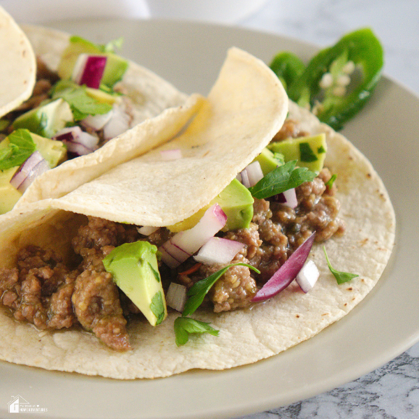 A taco filled with Salsa Verde Beef Filling, garnished with diced red onion, fresh cilantro, and avocado slices on a plate.