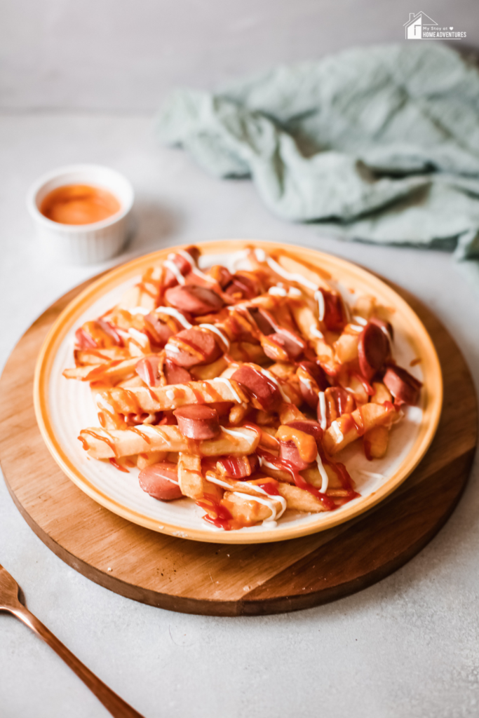 A plate of Salchipapas, a popular Peruvian dish made with crispy fries and sliced sausage, drizzled with ketchup and mayonnaise.