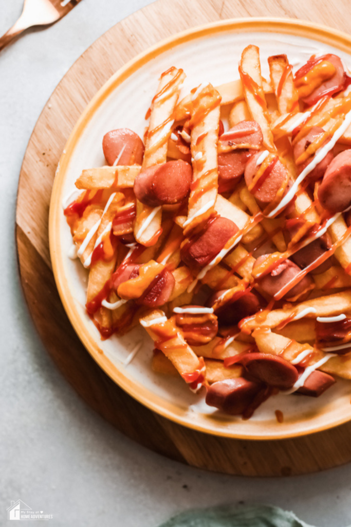 A close-up of Salchipapas, a Peruvian street food dish featuring crispy fries topped with sliced sausage, ketchup, and mayonnaise.