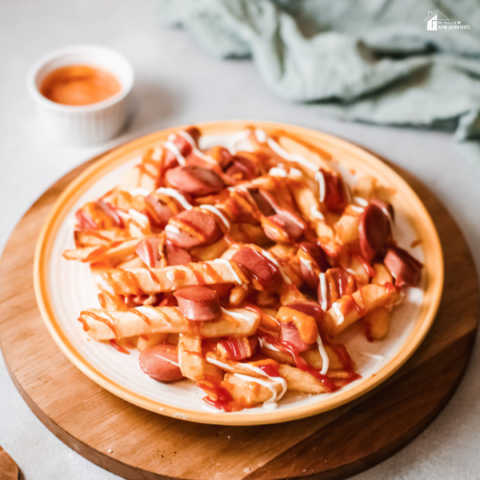 A plate of Salchipapas, a popular Peruvian dish made with crispy fries and sliced sausage, drizzled with ketchup and mayonnaise.