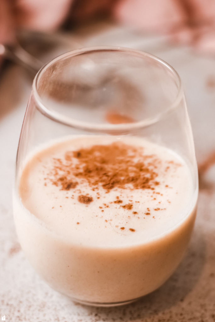 A close-up of a glass of creamy Rompope, a traditional Mexican holiday drink, topped with a dusting of cinnamon, perfect for festive Christmas gatherings.