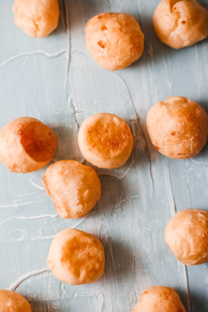 Top view of several golden Pan de Yuca, traditional Colombian cheese bread rolls made with yuca flour, displayed on a light blue surface, highlighting their crisp exterior and soft texture, ideal for gluten-free baking.