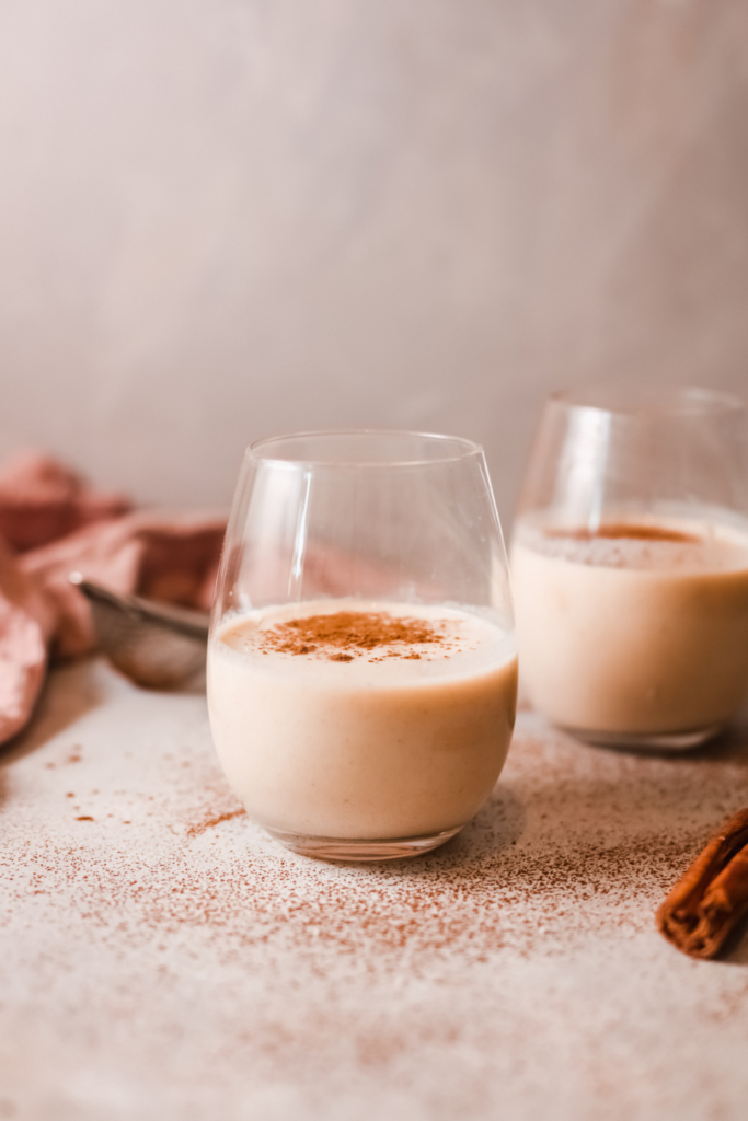 Two glasses of creamy homemade Rompope, a traditional Mexican holiday drink, topped with cinnamon, set on a festive table, ideal for Christmas and holiday celebrations.