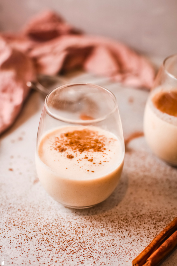 A glass of creamy homemade Rompope, a traditional Mexican holiday drink, topped with cinnamon, sitting on a festive table, perfect for Christmas and holiday celebrations.