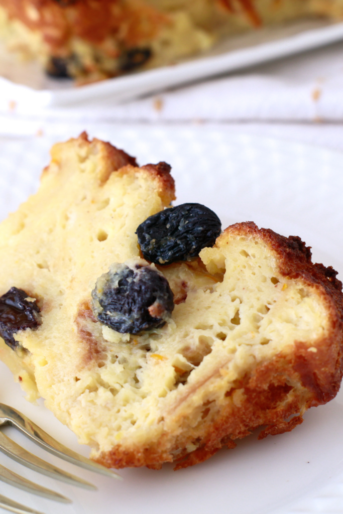 A close-up of a golden, custardy slice of Budín de Pan, a classic Puerto Rican bread pudding, with plump raisins and a crispy caramelized crust.