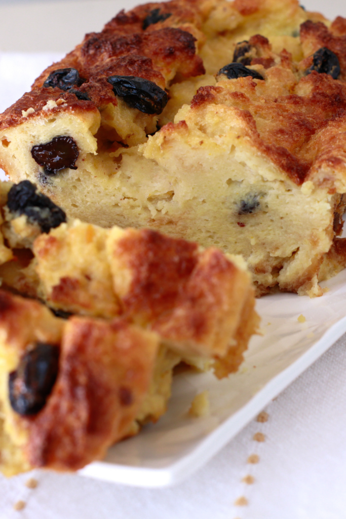 A freshly baked Budín de Pan, a traditional Puerto Rican bread pudding, with a golden, crispy crust and plump raisins, served on a white platter.