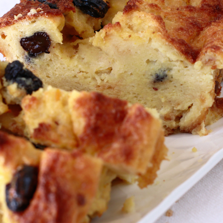 A freshly baked Budín de Pan, a traditional Puerto Rican bread pudding, with a golden, crispy crust and plump raisins, served on a white platter.