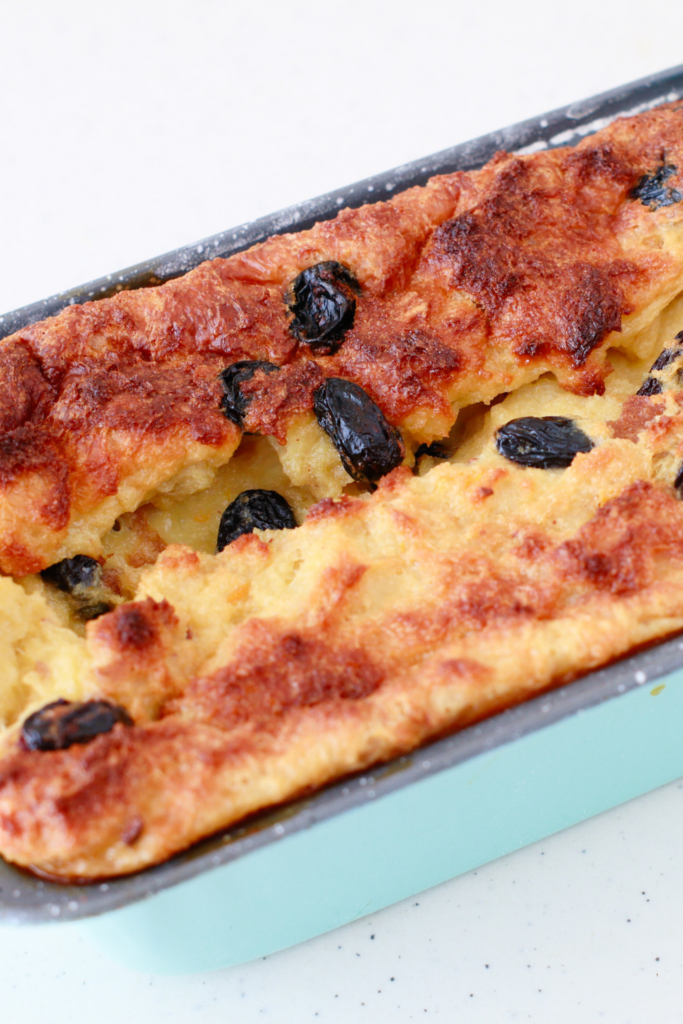 A freshly baked homemade Budín de Pan, a Puerto Rican bread pudding, with a golden-brown crust, plump raisins, and a soft custard interior in a baking dish.