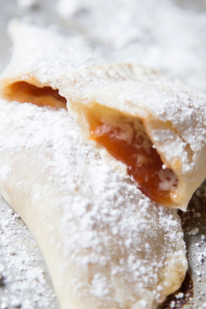 Close-up of a baked guava and cheese empanada dusted with powdered sugar, showing the sweet guava filling and flaky crust, perfect for a quick dessert or snack.