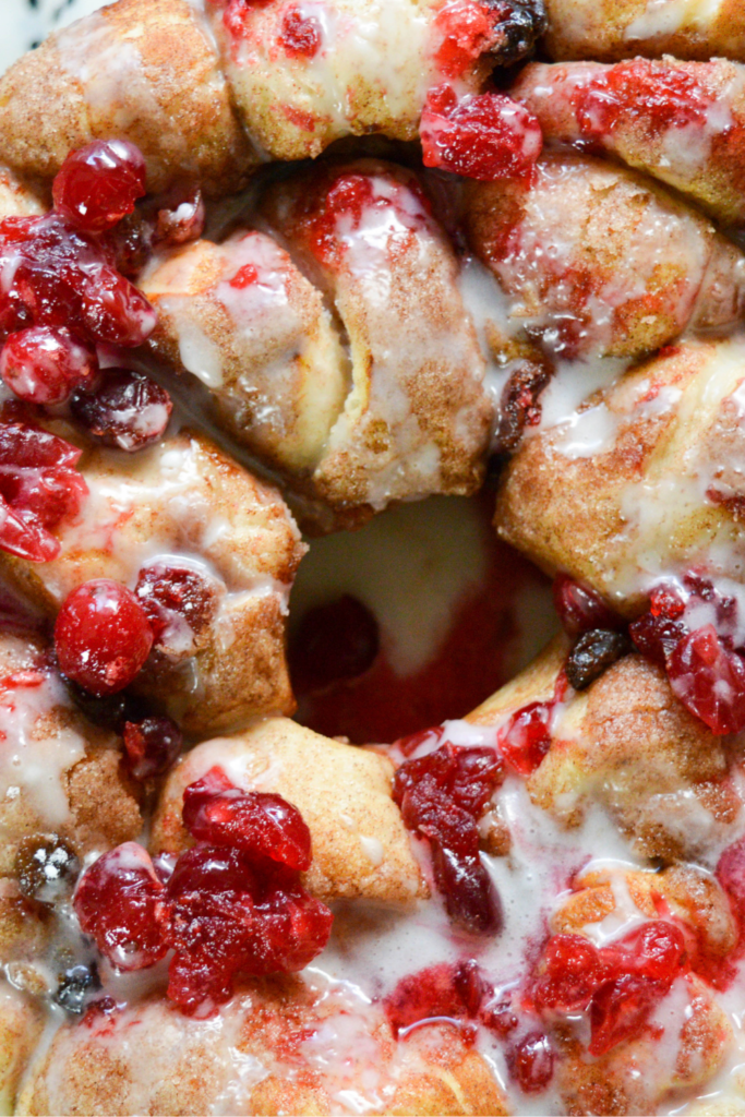 Close-up of cranberry raisin monkey bread drizzled with a sweet glaze, showcasing vibrant cranberries on a golden, cinnamon-sugar crust—ideal for holiday baking and christmas breakfast.