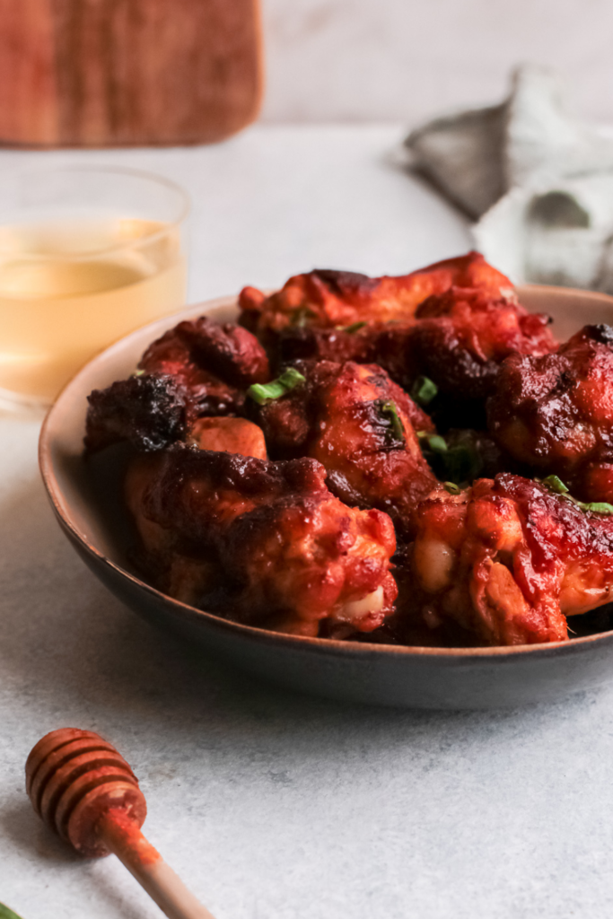 A plate of crispy bourbon honey air fryer chicken wings coated in a sticky, caramelized glaze, garnished with green onions, served with a glass of bourbon and a honey dipper, perfect for easy air fryer recipes and game day appetizers.