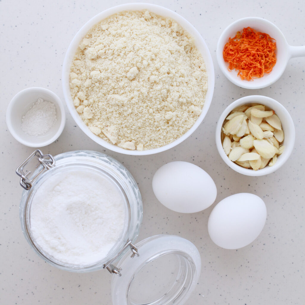 A collection of ingredients for Greek Almond Cookies, including almond flour, sugar, orange zest, eggs, and slivered almonds, perfect for a gluten-free cookie recipe.