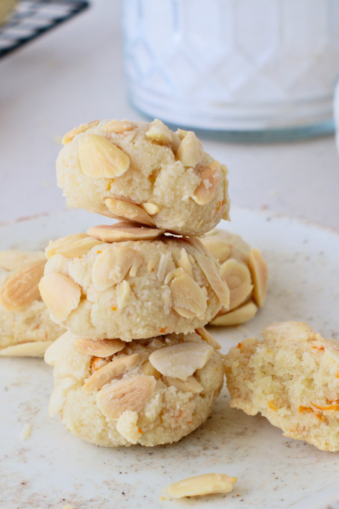 A stack of Greek Almond Cookies topped with slivered almonds and orange zest, showcasing their crumbly texture and golden edges, perfect for a gluten-free snack or dessert.