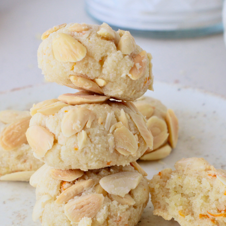 A stack of Greek Almond Cookies topped with slivered almonds and orange zest, showcasing their crumbly texture and golden edges, perfect for a gluten-free snack or dessert.