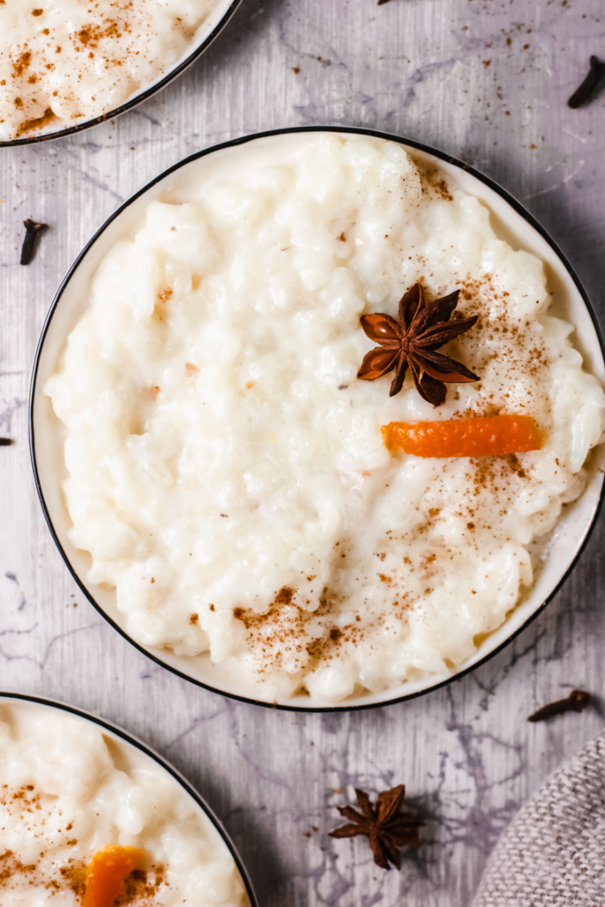 Close-up of a bowl of creamy Puerto Rican Arroz con Leche, garnished with cinnamon, orange peel, and star anise, showcasing the traditional rice pudding as a comforting holiday dessert or classic Latin American treat.