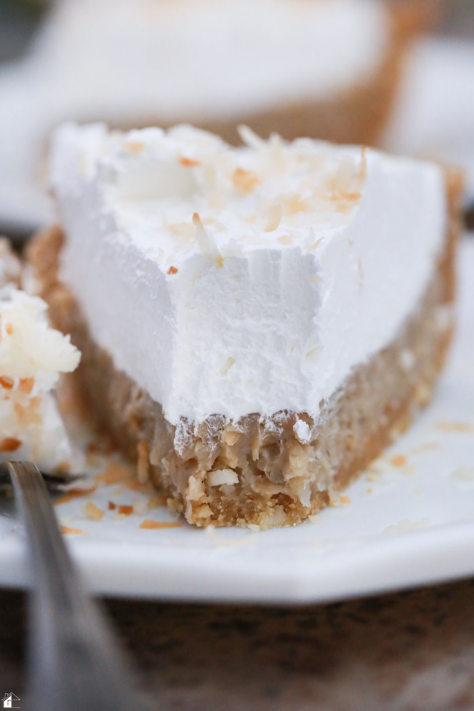 A close-up of a slice of Coconut Rum (Coquito) Cream Pie, featuring a creamy coconut filling, graham cracker crust, and topped with whipped cream and toasted coconut, perfect for holiday desserts and Puerto Rican-inspired recipes.