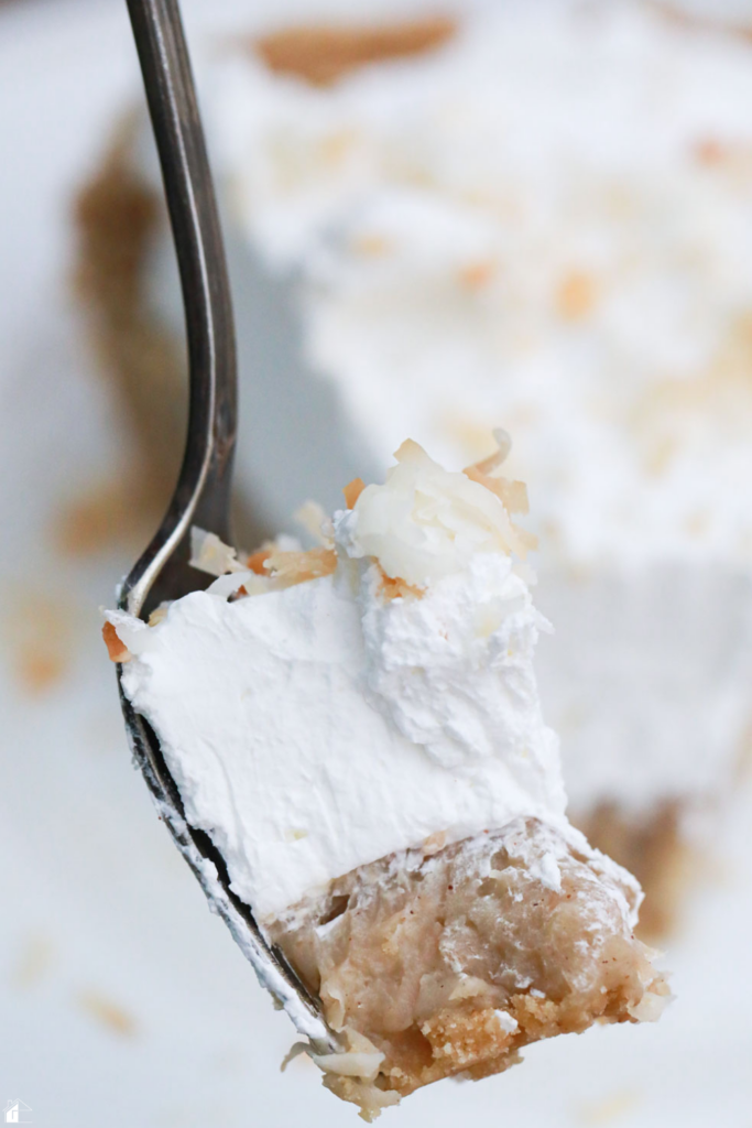 A close-up forkful of Coconut Rum (Coquito) Cream Pie, showcasing layers of creamy coconut filling, graham cracker crust, and whipped cream, topped with toasted coconut, ideal for holiday desserts and Puerto Rican-inspired pie recipes.