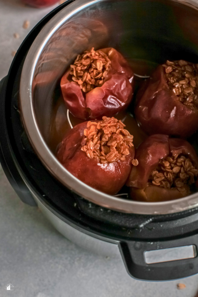 Four apples stuffed with oats and cinnamon, cooking inside an Instant Pot, ideal for a quick and healthy fall dessert.