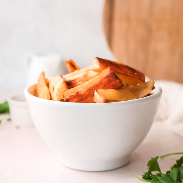 Bowl of golden, crispy baked yuca fries, perfectly cooked and ready to serve as a gluten-free snack or side dish, with a touch of fresh herbs in the background.