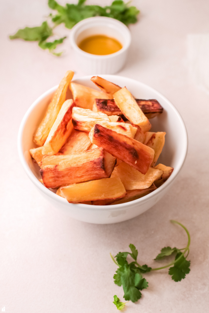 Bowl of golden, crispy baked yuca fries, served with a side of oil and garnished with fresh cilantro, ready to enjoy as a gluten-free snack or side dish.