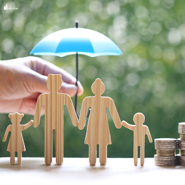 An image of a wooden family figurines, with coins on the side and a blue umbrella behind.