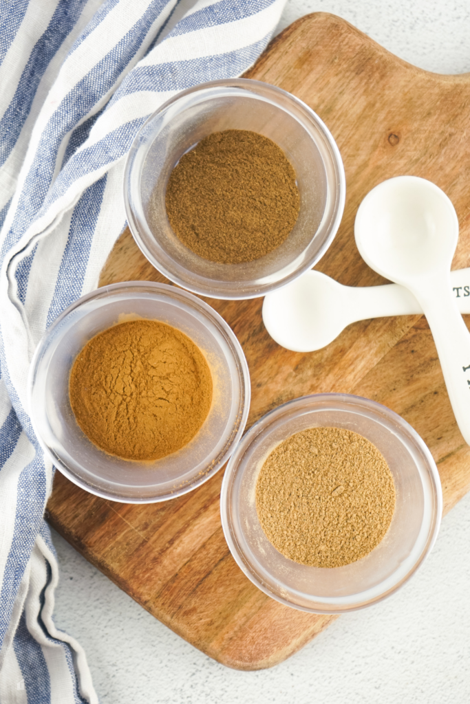 Three small bowls of ground spices ready to be mixed for an apple pie seasoning recipe. Learn how to make apple pie spice for fall dessert ideas and homemade dry mixes like this pie spice recipe.