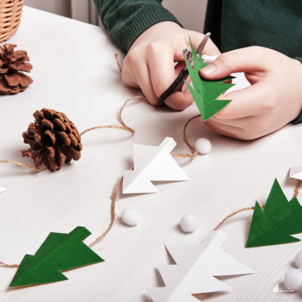 A person creating DIY Christmas tree garland with paper and twine, highlighting cheap Christmas activities for families to stay within a budget.