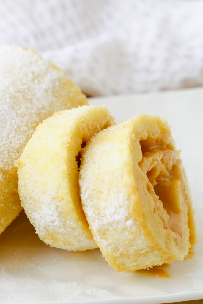 Close-up of a fluffy Brazo Gitano (Swiss Roll) filled with creamy dulce de leche, dusted with powdered sugar, showcasing the golden sponge and rich caramel filling.