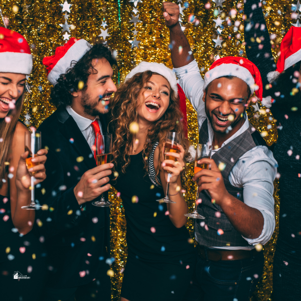 A cheerful group of colleagues wearing Santa hats and formal attire enjoying a Christmas party with champagne and golden decorations, highlighting holiday fashion ideas.