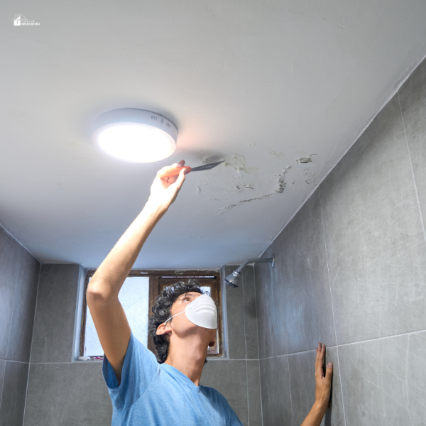 A man wearing a protective mask repairing a ceiling with visible damage, demonstrating home maintenance as part of winter pest control strategies.