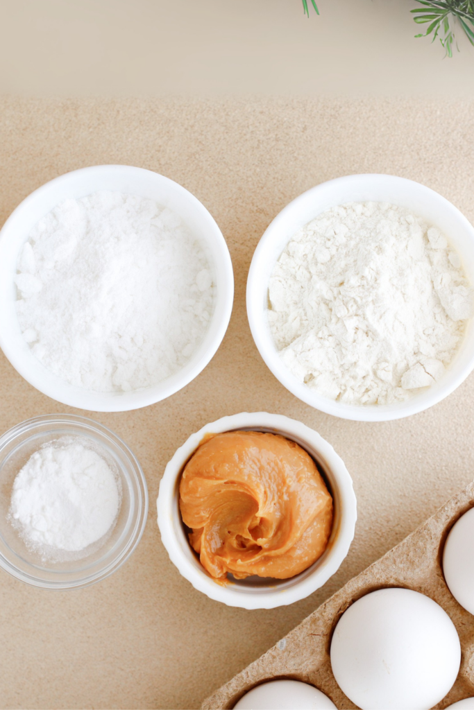 Ingredients for Brazo Gitano (Swiss Roll) recipe, including bowls of flour, sugar, baking powder, and creamy dulce de leche, alongside fresh eggs on a neutral background.