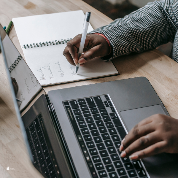 A person writing notes in a planner next to a laptop, showcasing organization tips for busy parents managing an electrical career and family responsibilities.