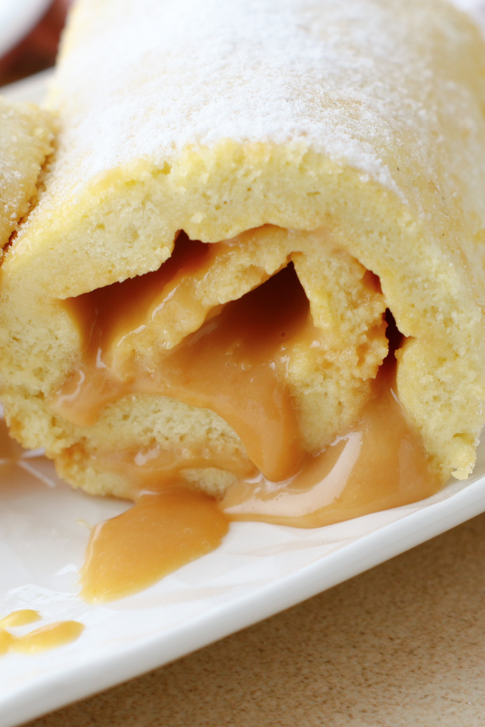 Close-up of a Brazo Gitano (Swiss Roll) filled with creamy dulce de leche, showcasing its soft sponge texture and rich caramel filling oozing out, dusted with powdered sugar.