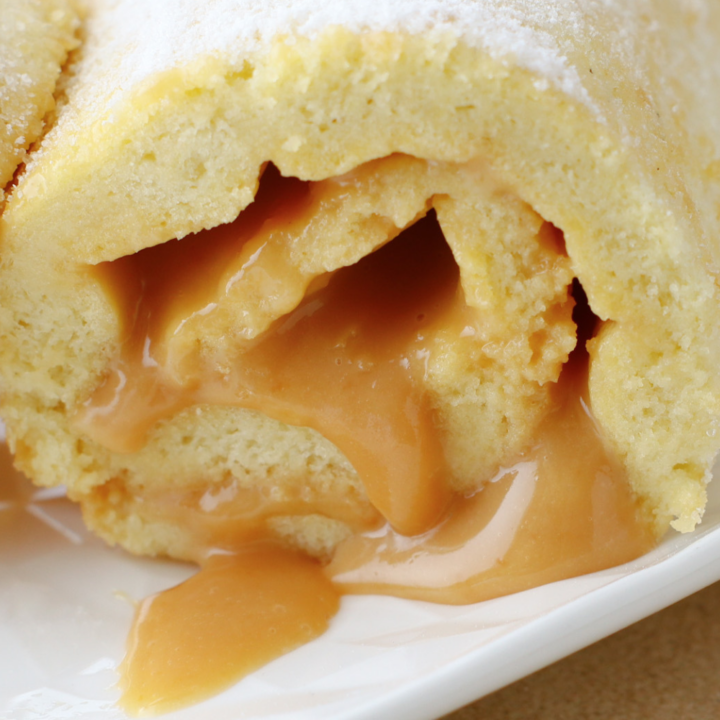 Close-up of a Brazo Gitano (Swiss Roll) filled with creamy dulce de leche, showcasing its soft sponge texture and rich caramel filling oozing out, dusted with powdered sugar.