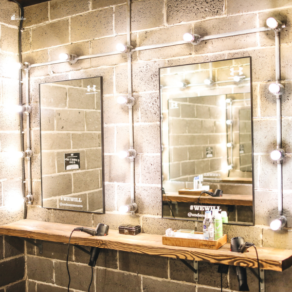 A rustic vanity setup with two rectangular mirrors surrounded by exposed lightbulbs against a brick wall.