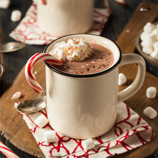 A mug of rich hot chocolate topped with whipped cream and a candy cane, surrounded by marshmallows, offering a cozy winter drink idea.