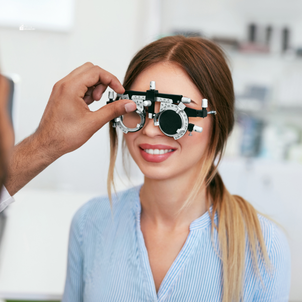 A smiling woman undergoing an eye exam with a trial frame, highlighting affordable vision care solutions for maintaining healthy eyesight.