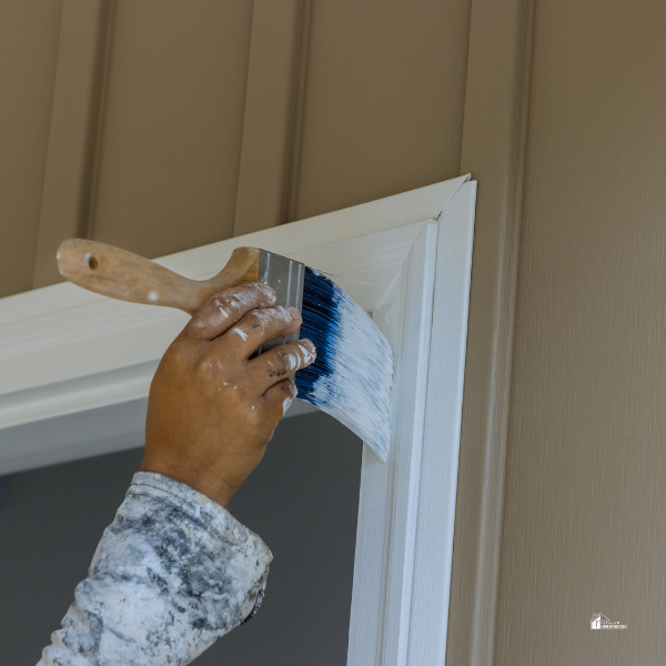 A person painting a white door frame with a brush, illustrating a DIY home improvement project.