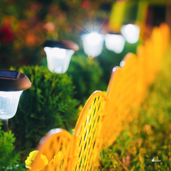 Solar-powered garden lights illuminating a landscaped yard with a yellow decorative fence in the foreground.