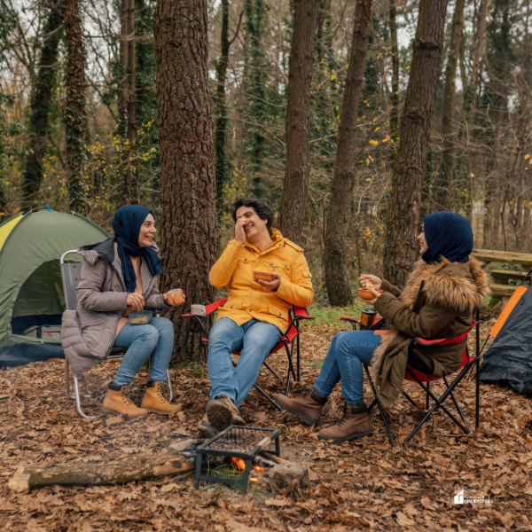 Three friends enjoying a meal and conversation around a campfire in a forested campsite, emphasizing the importance of having the right gear for cooking on a camping trip.