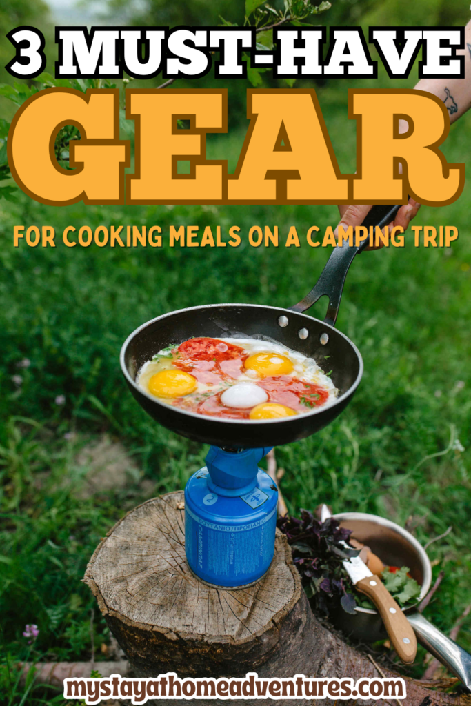 A portable camping stove cooking eggs and tomatoes in a pan, demonstrating essential gear for preparing meals outdoors.